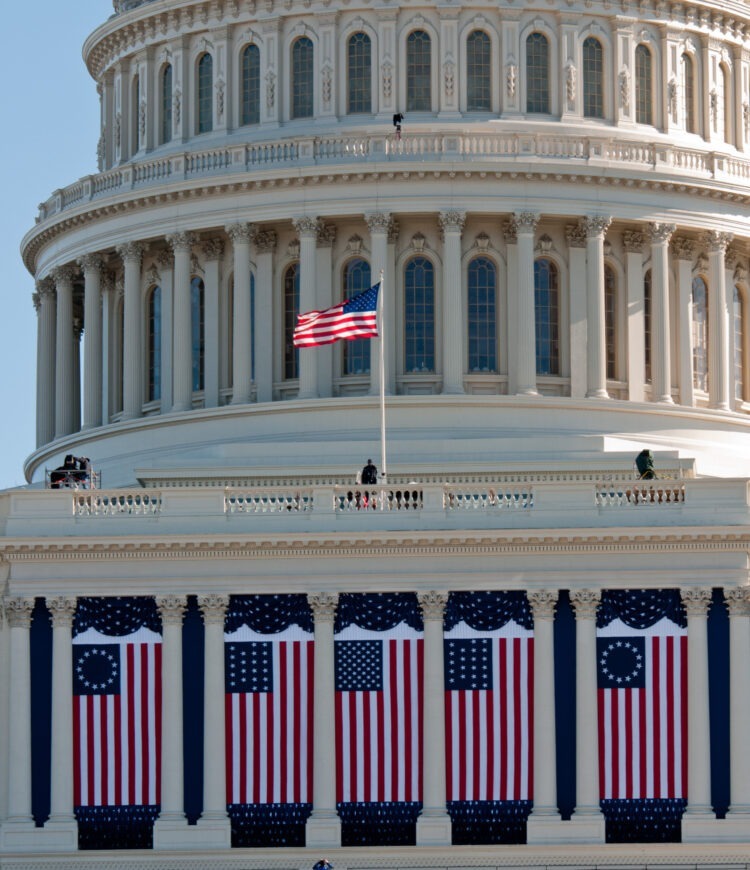 Flags hang from the United States Capitol building as preparations continue for the 57th Presidential Inauguration. Each hanging flag is from a different period in the country's history: 50-star flag in center; 21-star flags on either side (flown when Illinois joined the Union in 1818); 13-star Betsy Ross flags on far ends.