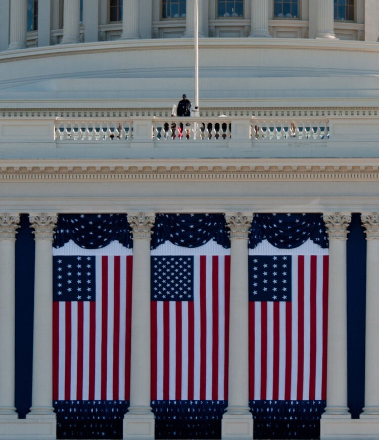 Flags hang from the United States Capitol building as preparations continue for the 57th Presidential Inauguration. Each hanging flag is from a different period in the country's history: 50-star flag in center; 21-star flags on either side (flown when Illinois joined the Union in 1818); 13-star Betsy Ross flags on far ends.