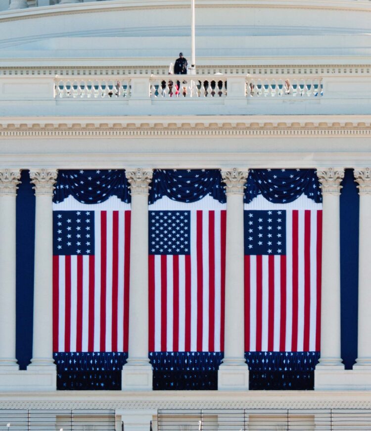 Flags hang from the United States Capitol building as preparations continue for the 57th Presidential Inauguration. Each hanging flag is from a different period in the country's history: 50-star flag in center; 21-star flags on either side (flown when Illinois joined the Union in 1818); 13-star Betsy Ross flags on far ends.