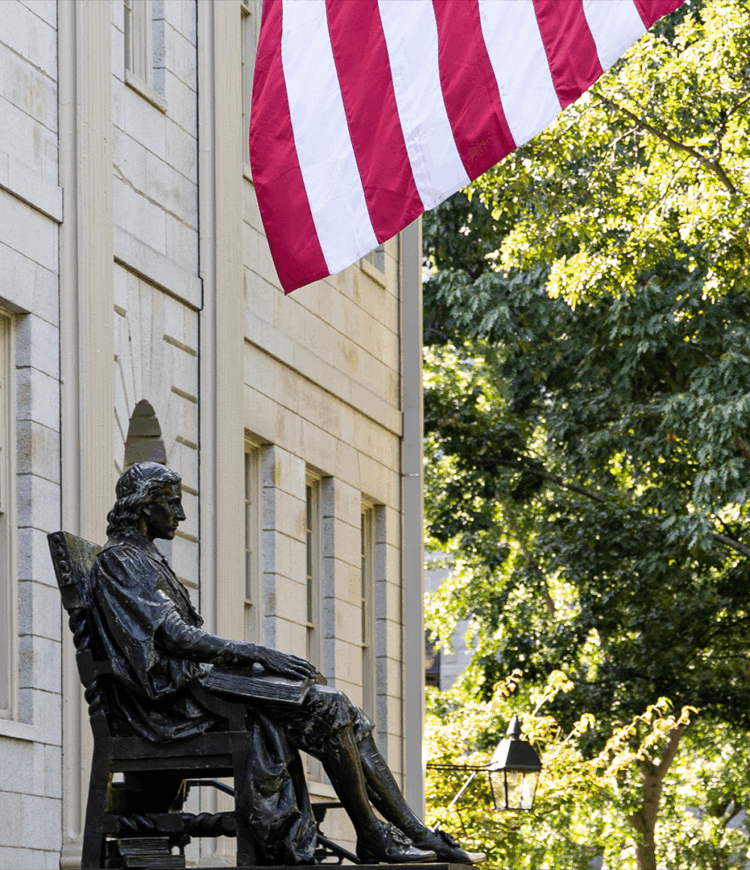 Statue of John Harvard in front of a building with an American flag hanging from the building