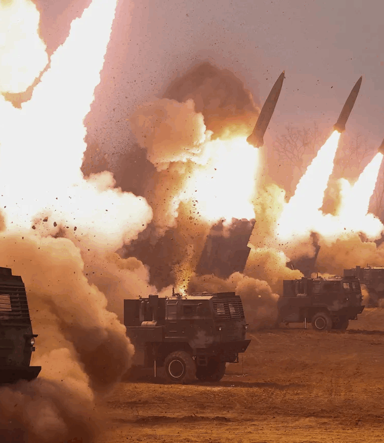 A number of heavy artillery trucks are parked in a row, launching missiles