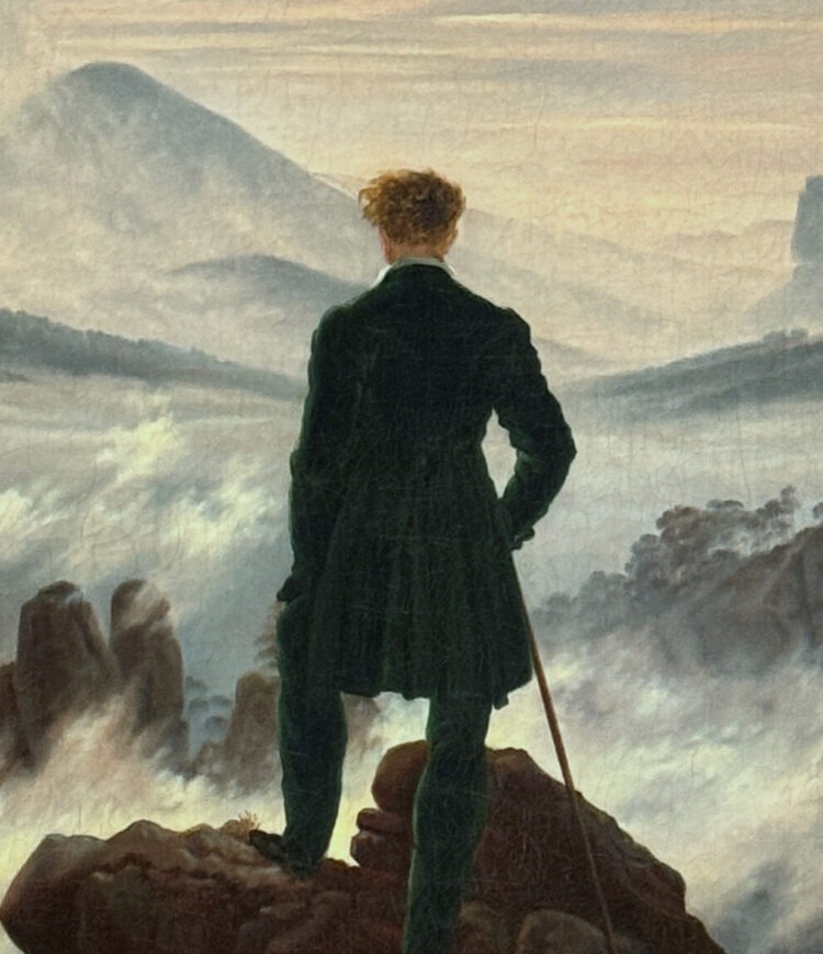 A man stands on a mountaintop, looking out at a fog-covered mountain range