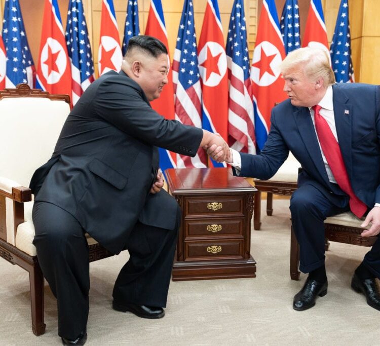 Kim Jong Un shakes hands with President Donald Trump, as they sit in front of North Korean and American flags