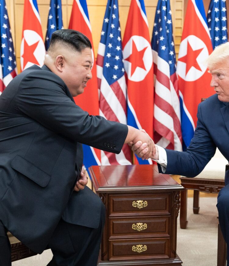 Kim Jong Un shakes hands with President Donald Trump, as they sit in front of North Korean and American flags