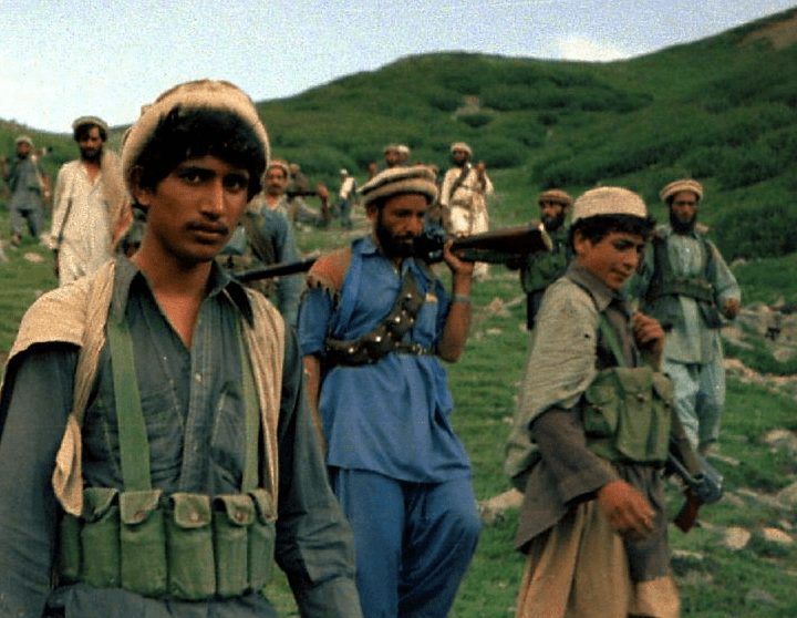 Afghan mujahideen walking down a green hillside