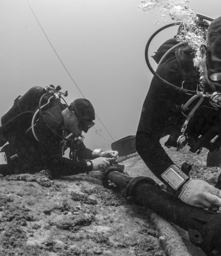 Two scuba divers working on equipment along the ocean floor.